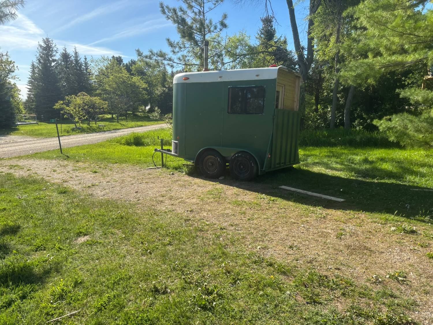 The Fire & Rein sauna trailer parked on a grassy lot among pine trees